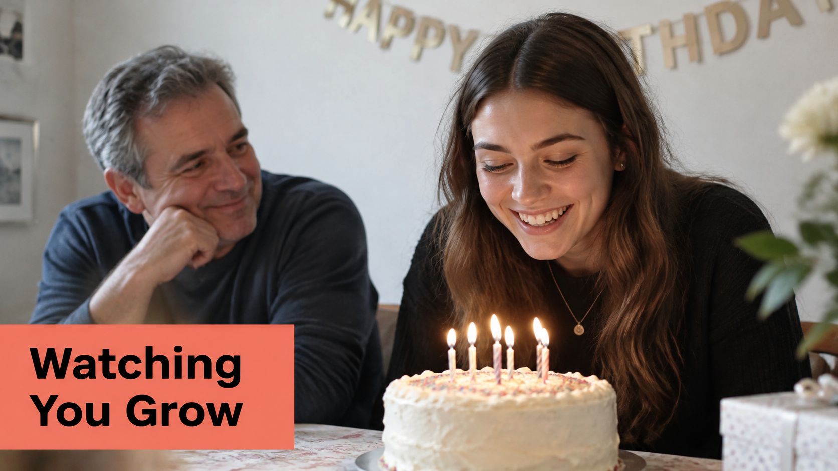 A father smiling warmly at his daughter as she prepares to blow out candles on a birthday cake.