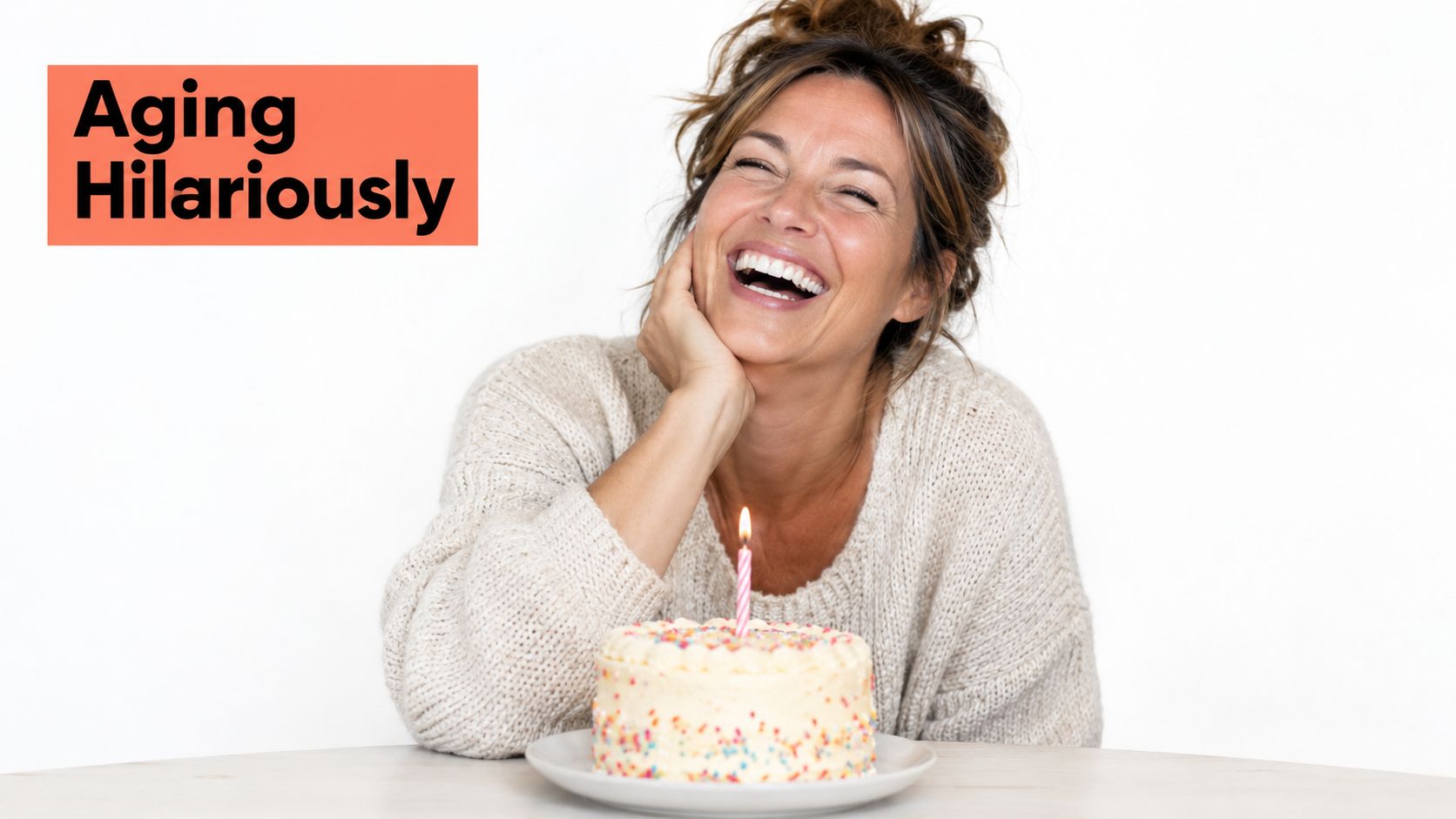 A happy middle-aged woman laughing while sitting in front of a small birthday cake with one candle.