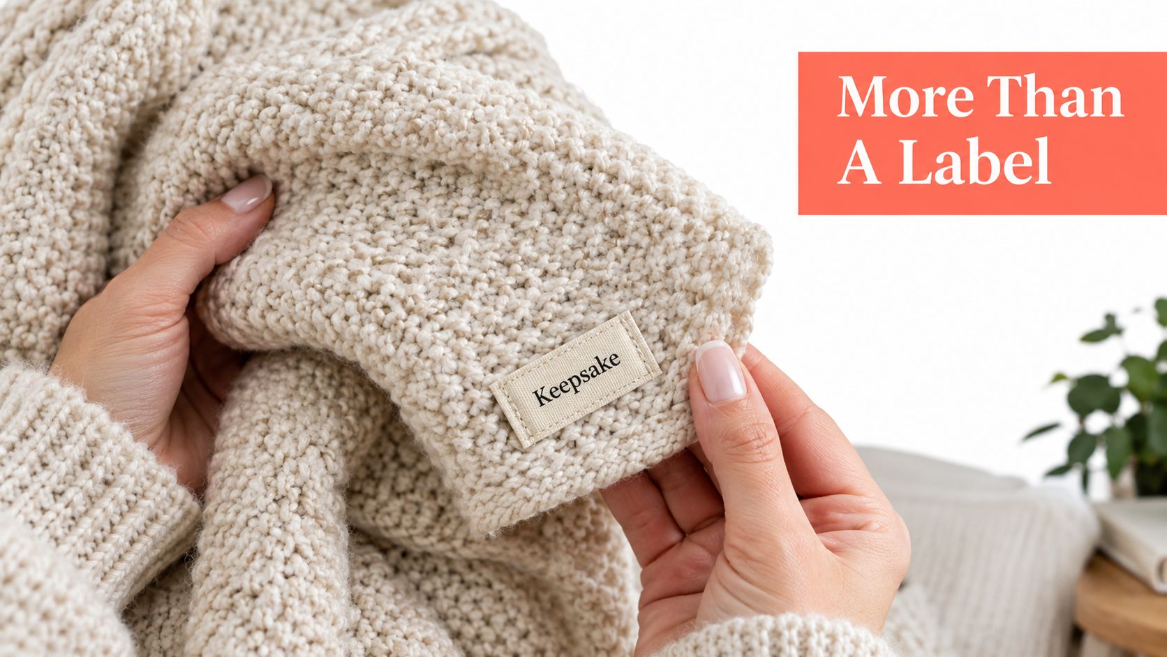 A close-up view of a person holding a beige knitted blanket featuring a woven label reading Keepsake.