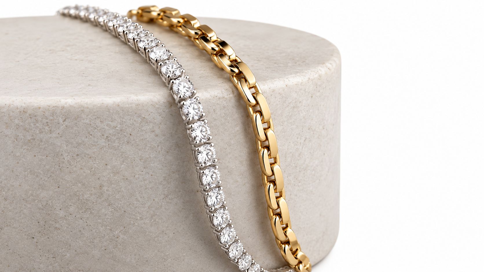 A silver diamond tennis bracelet and a gold chain bracelet resting on a beige stone display.