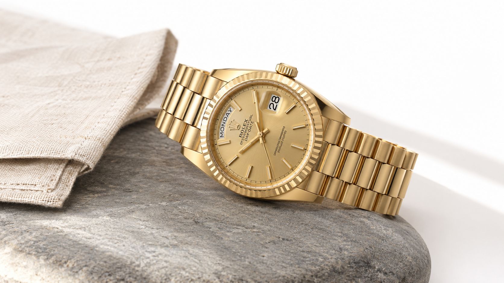 A luxurious gold Rolex Day-Date wristwatch resting elegantly on a smooth gray stone beside a linen cloth.