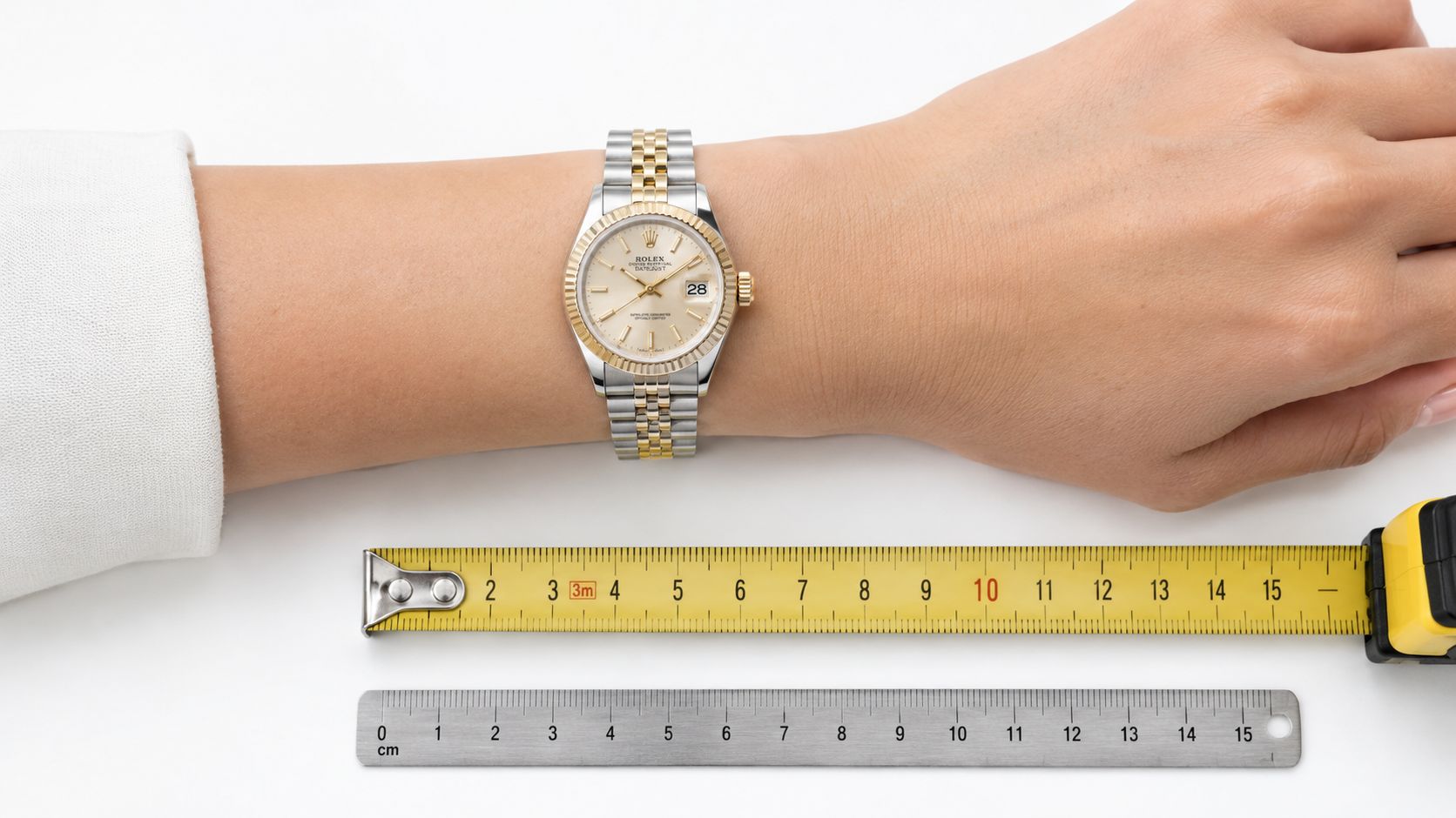 A gold and stainless steel Rolex Datejust watch worn on a person's wrist next to measuring tools.