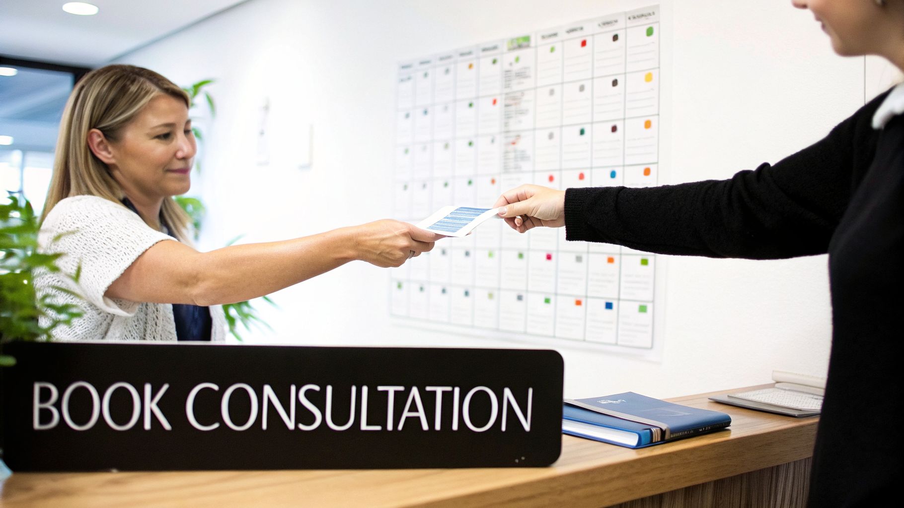 Two women exchange documents across a counter with a “Book Consultation” sign and a grid board.