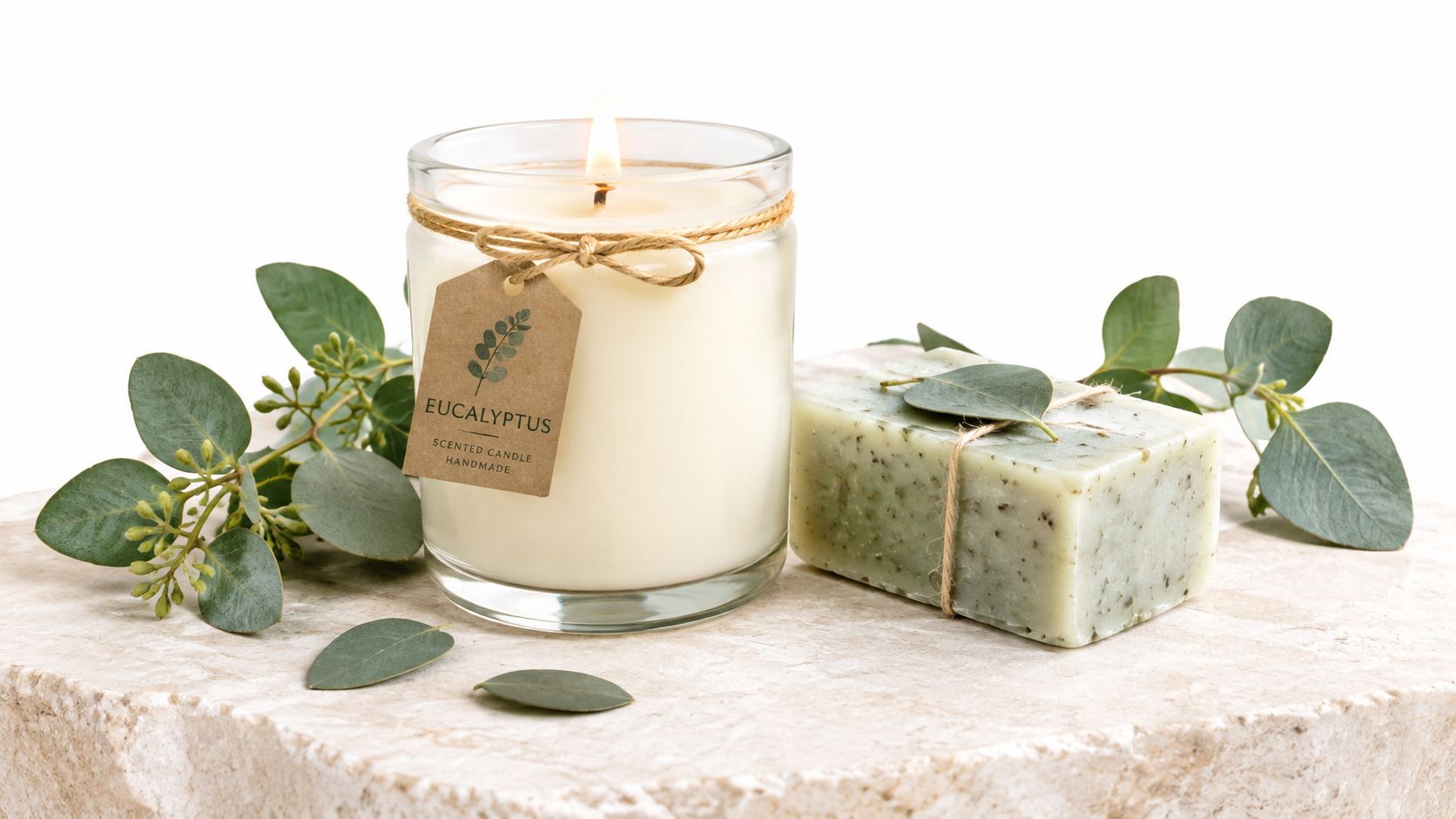 A scented eucalyptus candle and natural soap bar displayed on a stone surface with eucalyptus leaves.