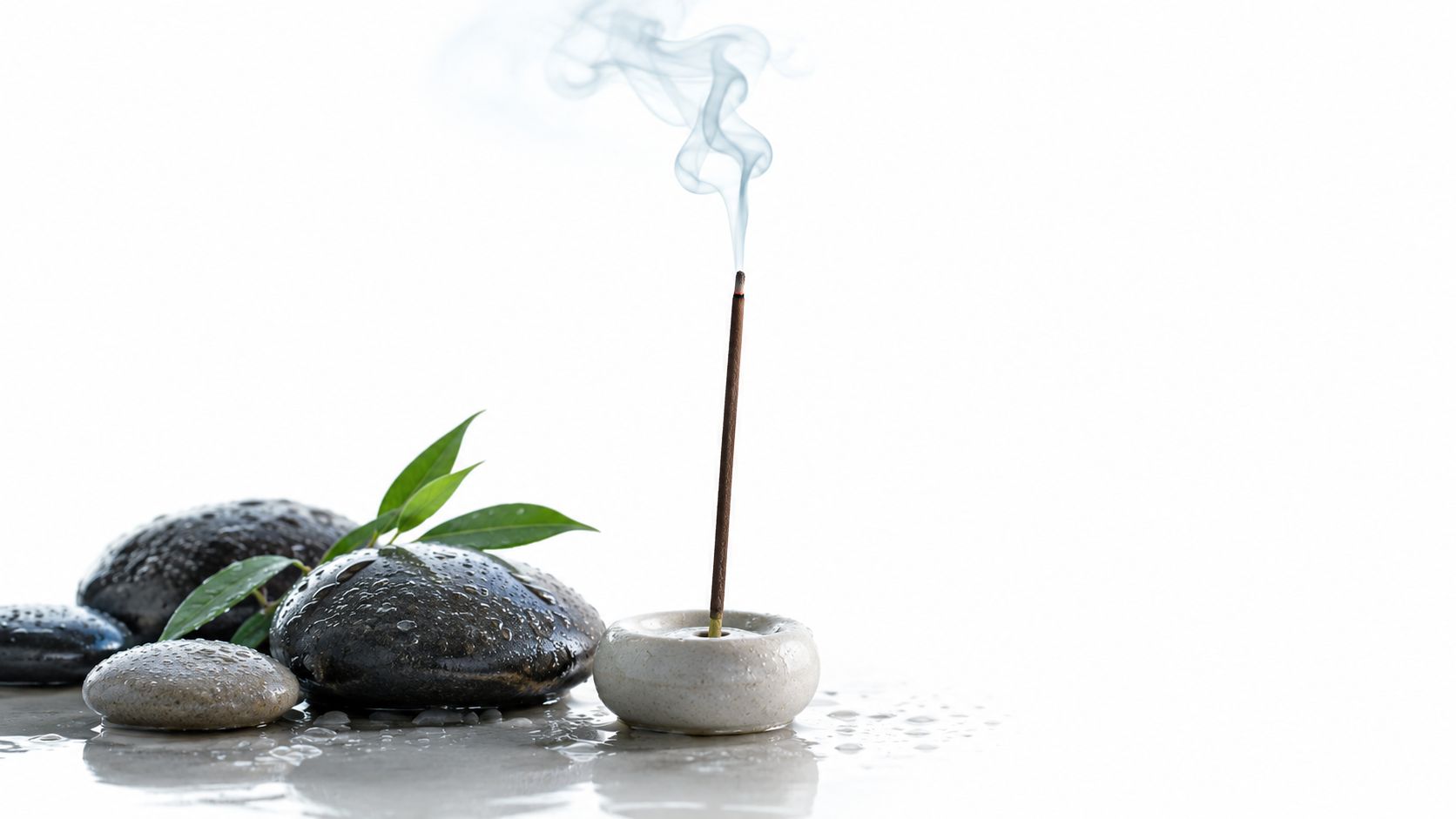 A lit incense stick emitting smoke next to wet zen stones and green bamboo leaves on water