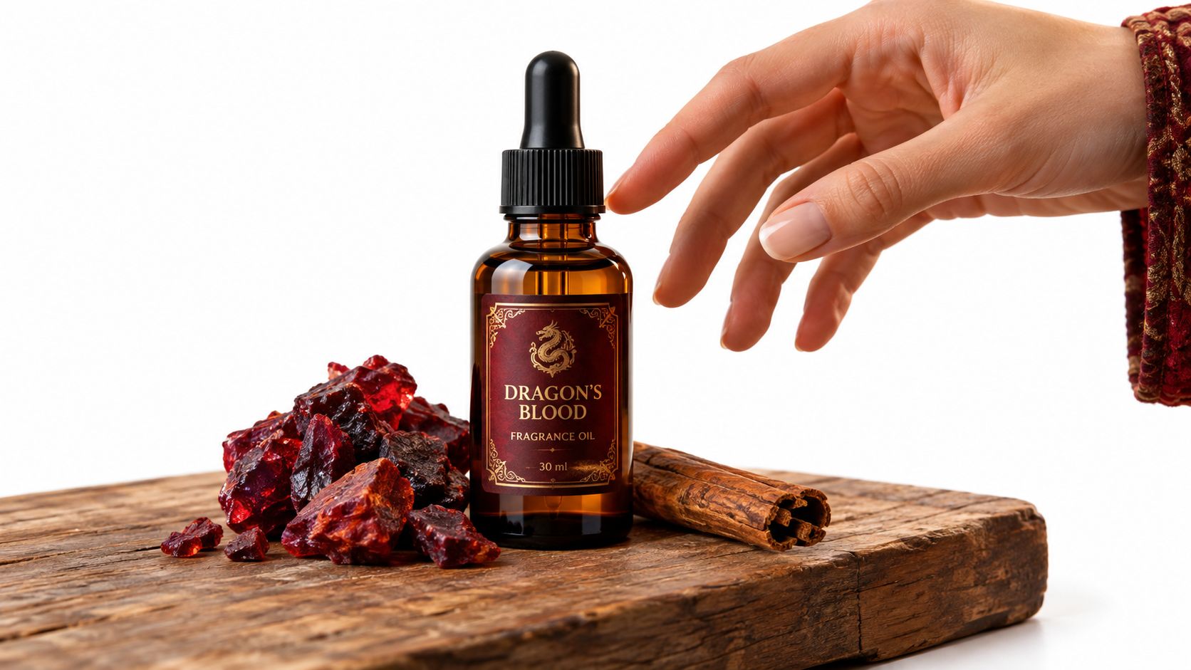A hand reaches toward a bottle of Dragon's Blood fragrance oil surrounded by resin chunks and cinnamon sticks.