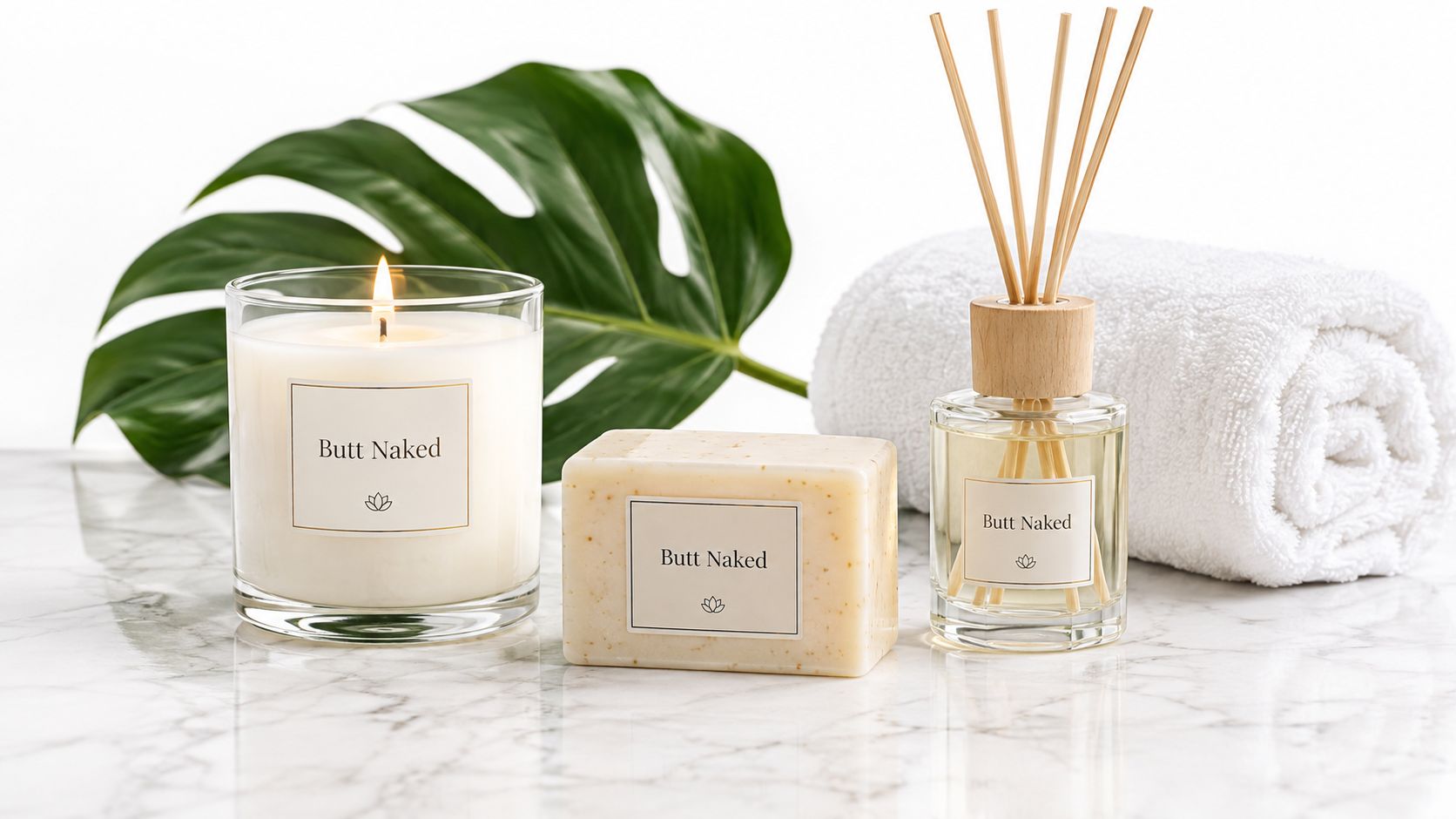 A scented candle, bar of soap, and reed diffuser on a marble surface with a green leaf.