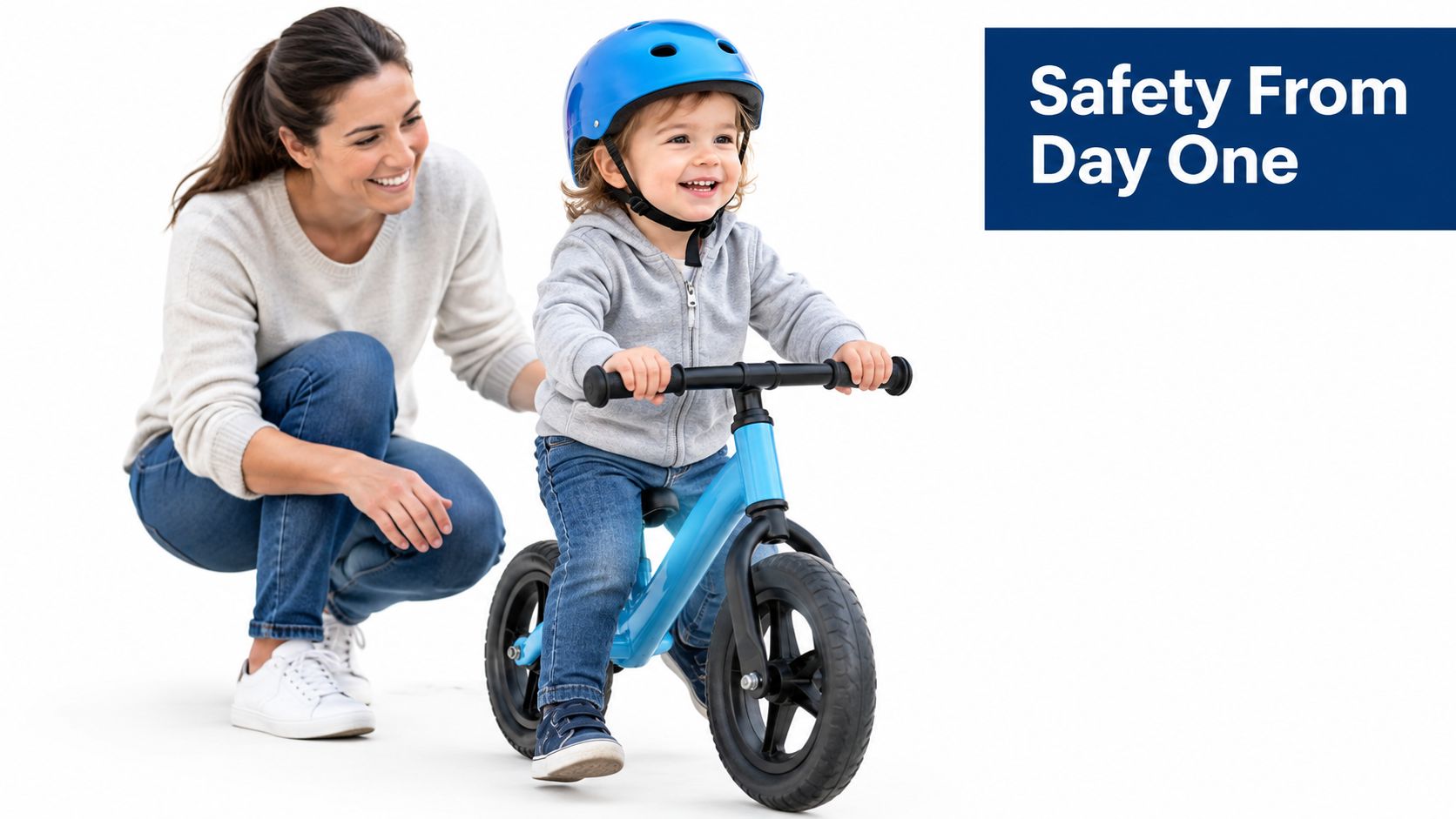 A smiling toddler wearing a blue safety helmet riding a blue balance bike while mom watches closely.