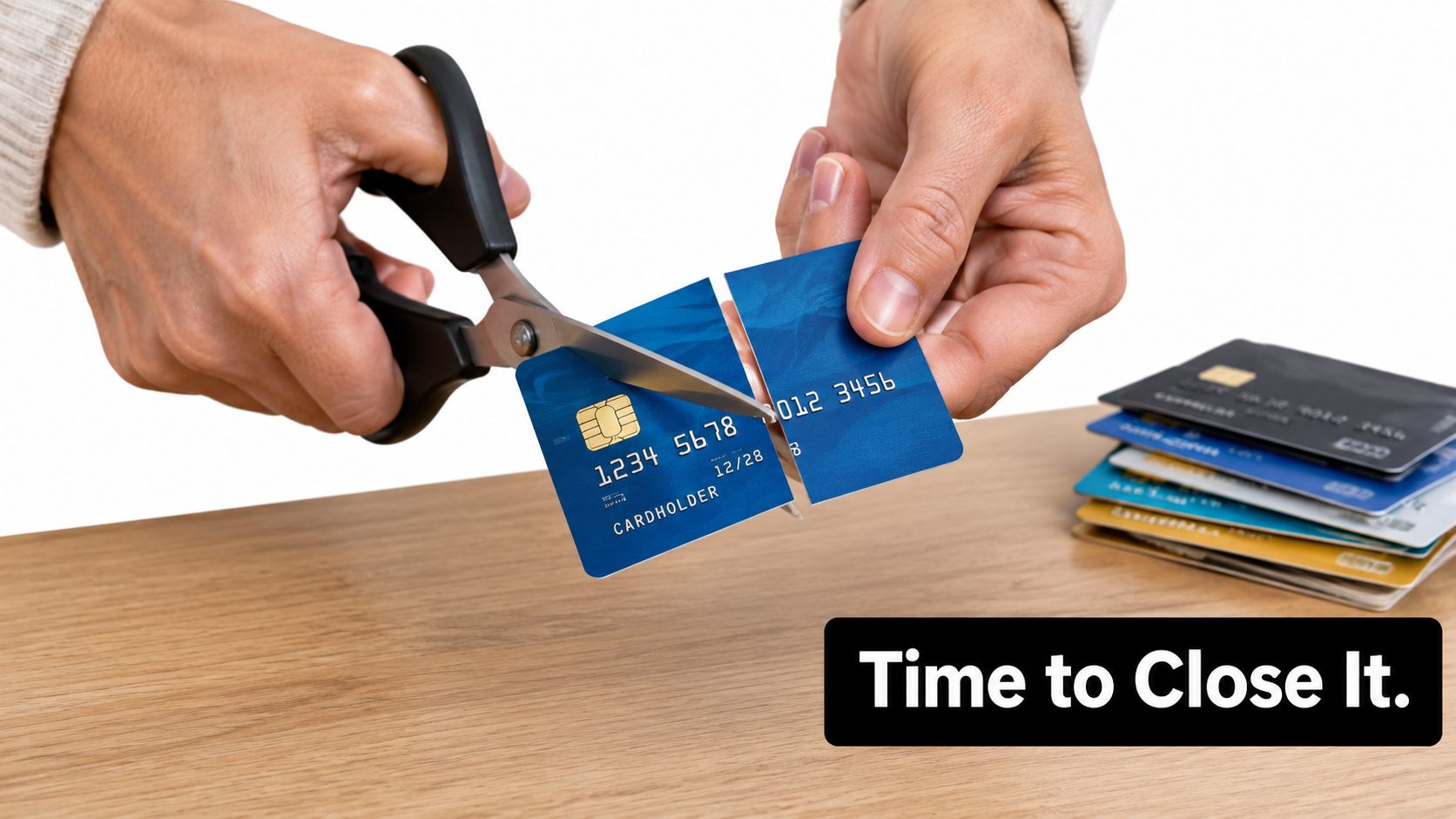 A person using scissors to cut a blue credit card in half on a wooden table.