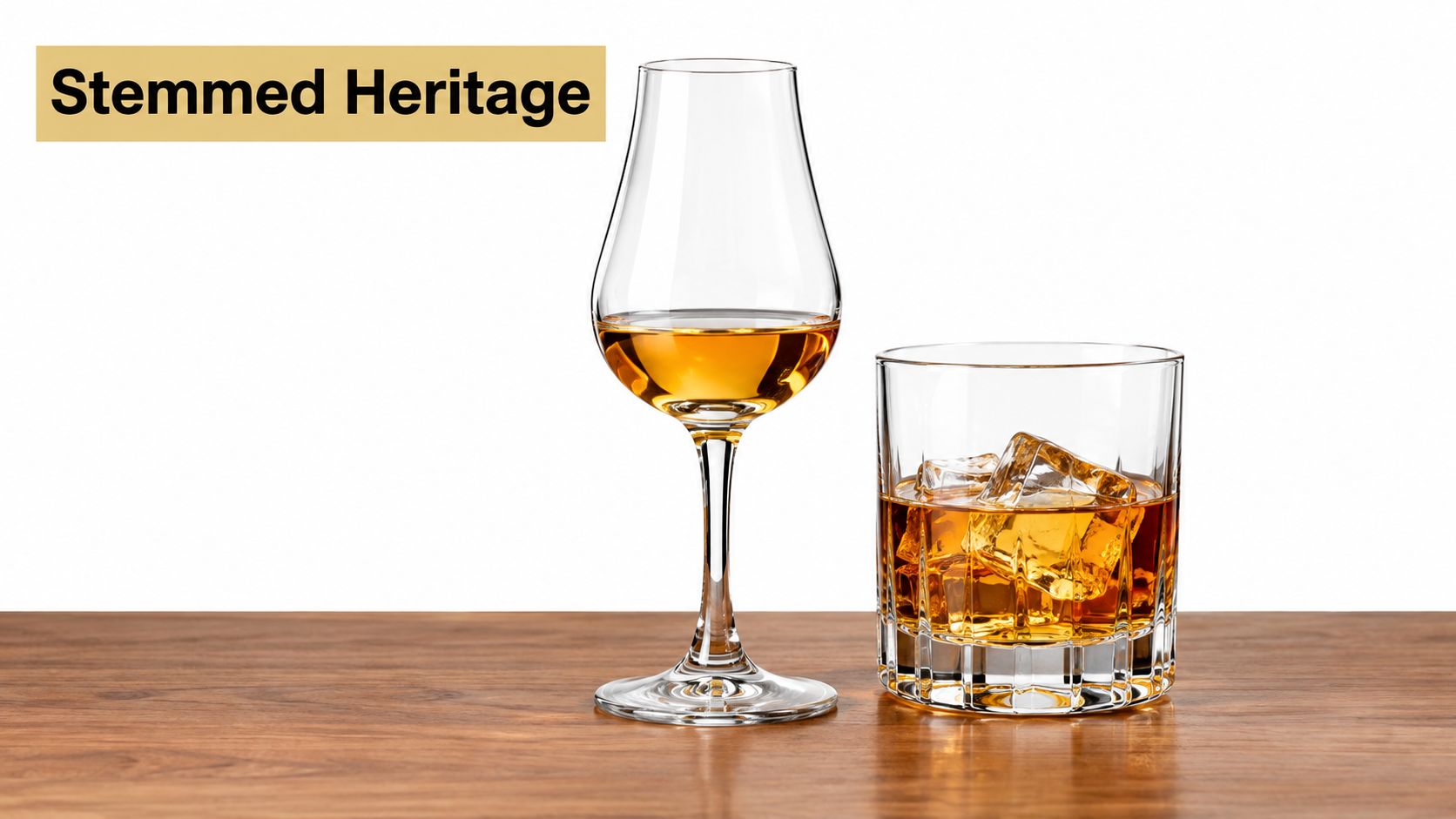 A stemmed tasting glass and a rocks glass filled with whiskey and ice on a wooden table.