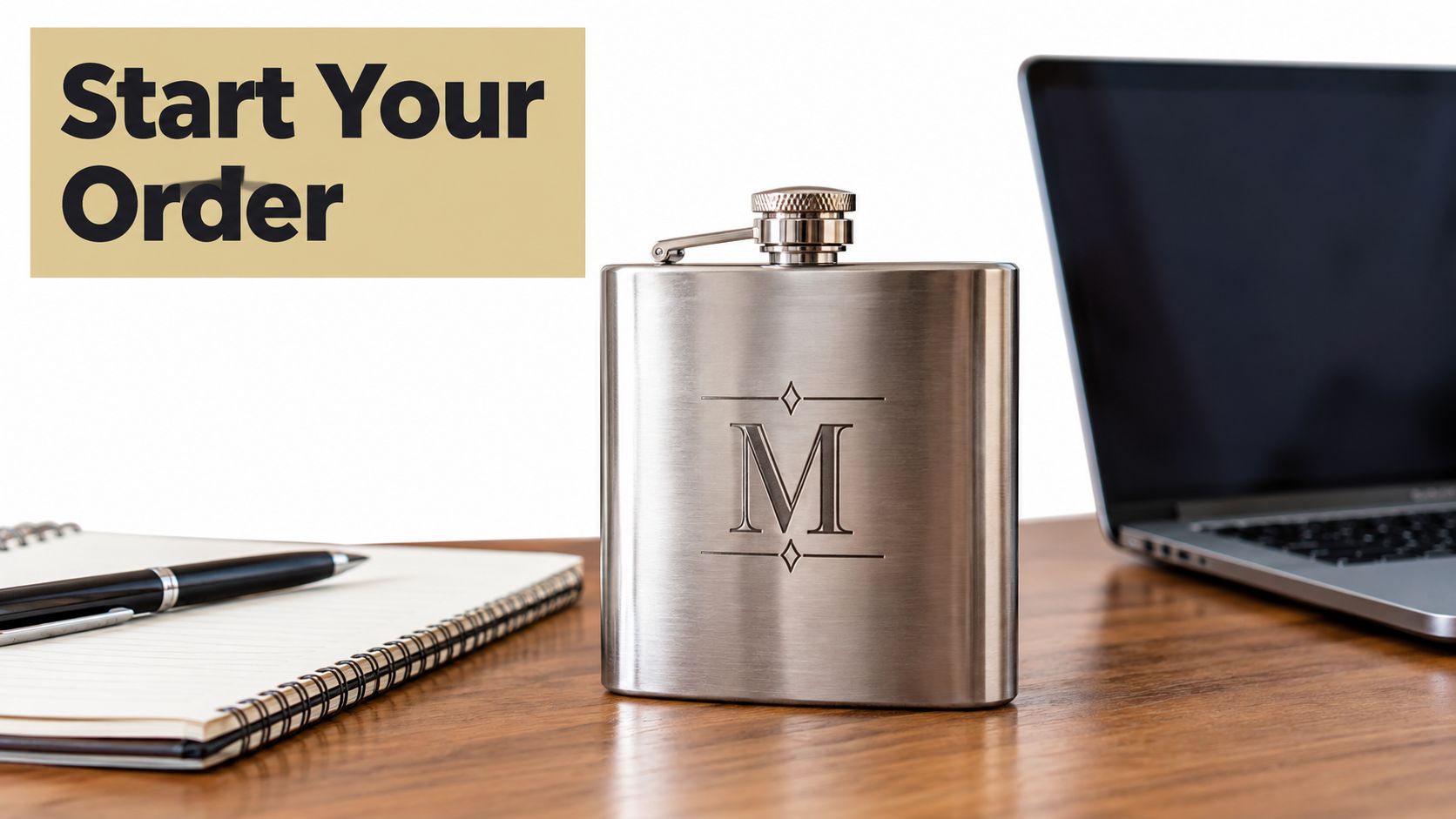 A stainless steel flask with a laser engraved monogram M sits on a wooden desk with a notebook.