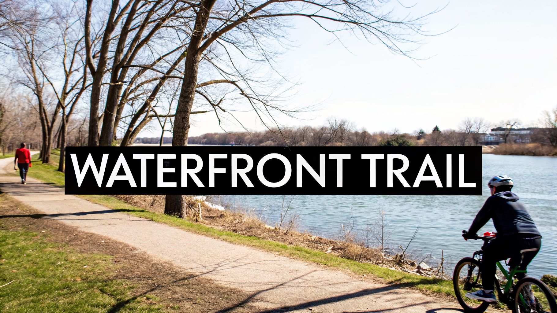 A scenic waterfront trail with a walker and a cyclist under bare trees beside a river.