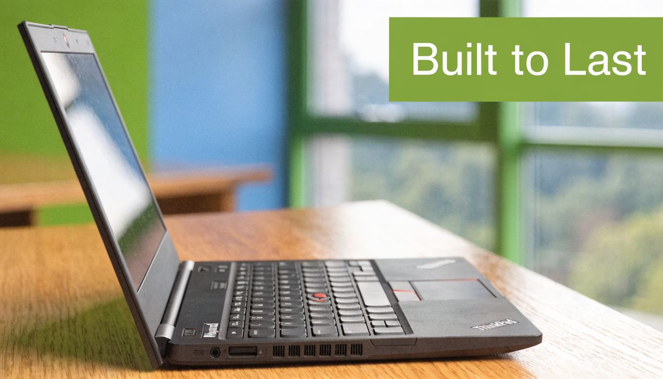 A black Lenovo ThinkPad laptop sits on a wooden desk near a blurred office window.