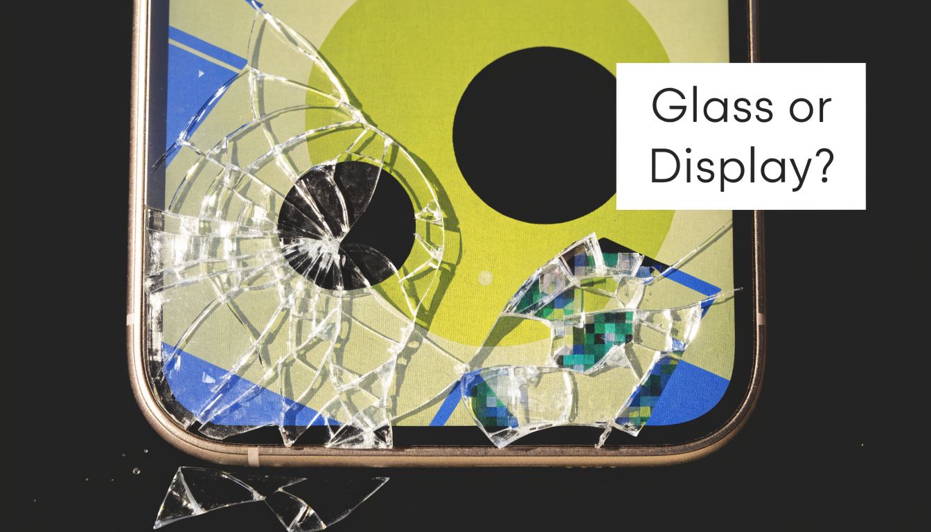 A close-up of a broken smartphone screen with visible cracks and shattered glass fragments lying below.