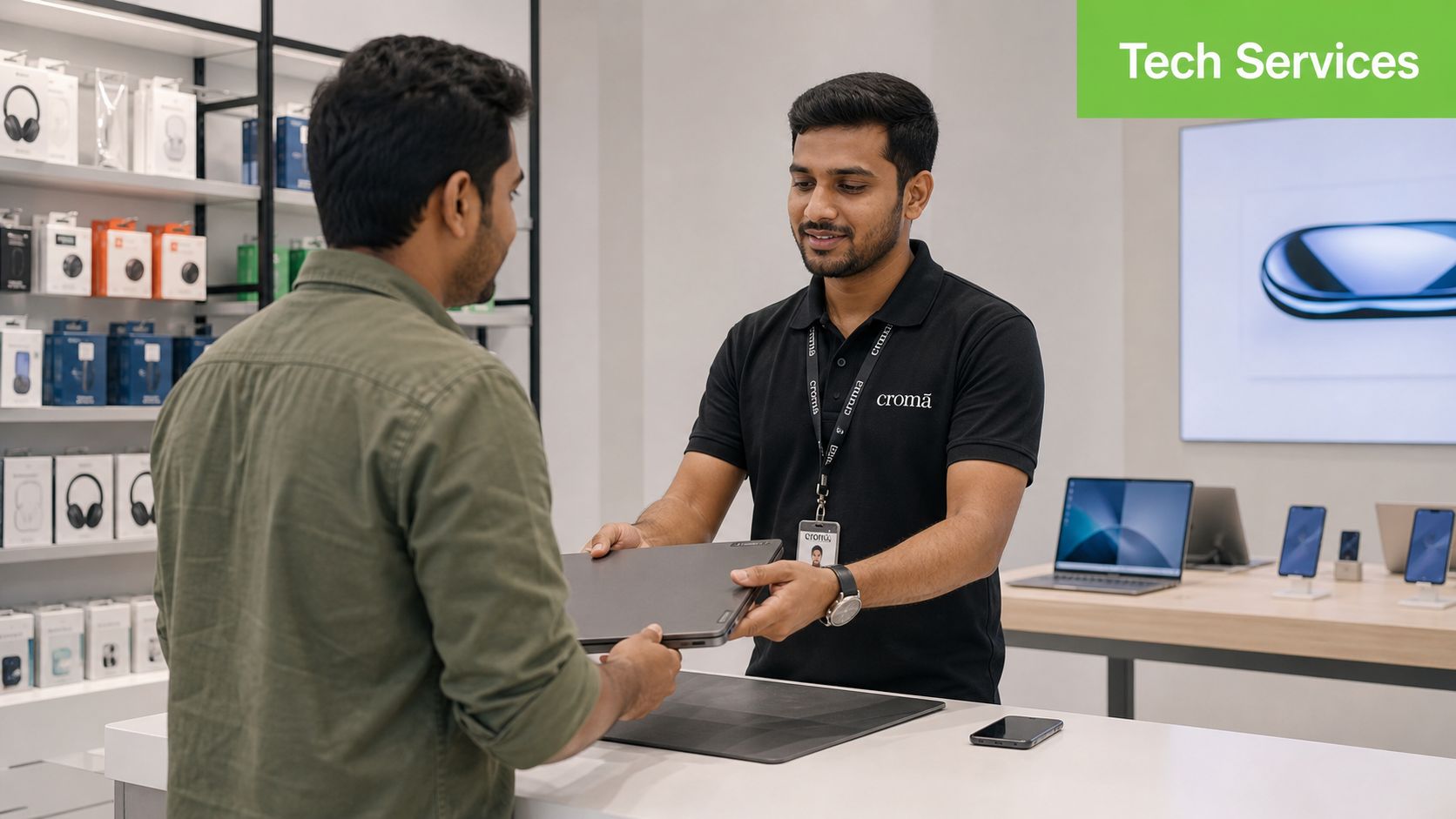 A store employee handing a laptop to a customer at a tech services counter in a store.