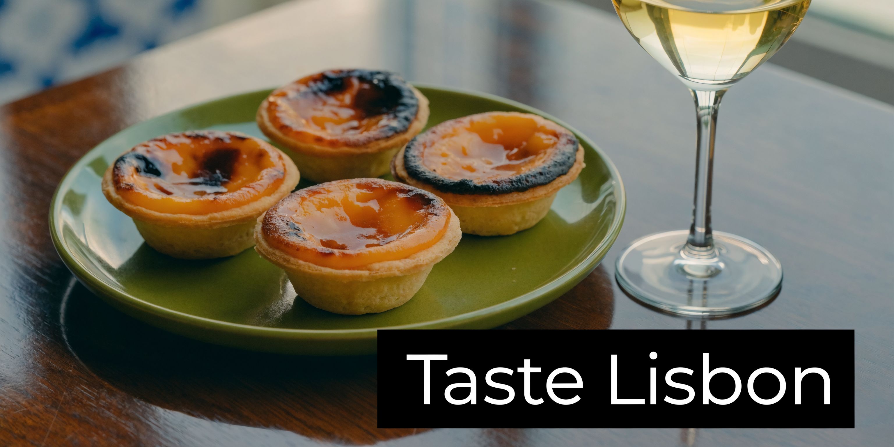 Four delicious Portuguese egg tarts served on a small green plate next to a glass of wine.