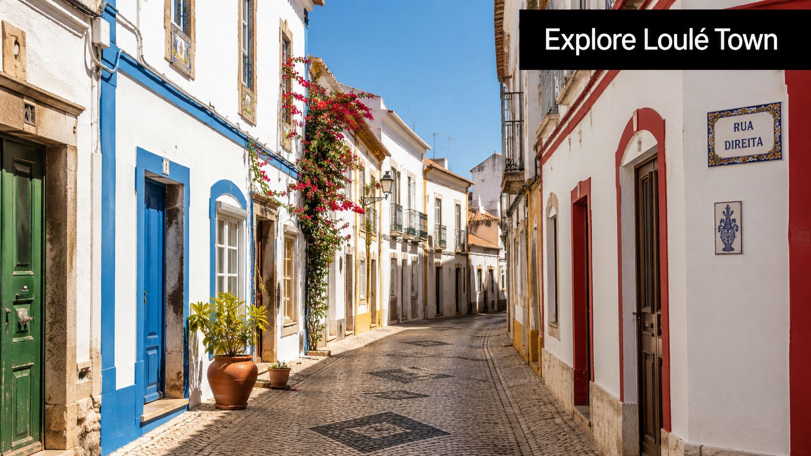 A scenic, narrow street in Loule, Portugal, featuring white buildings with colorful door frames and cobblestone pathways.