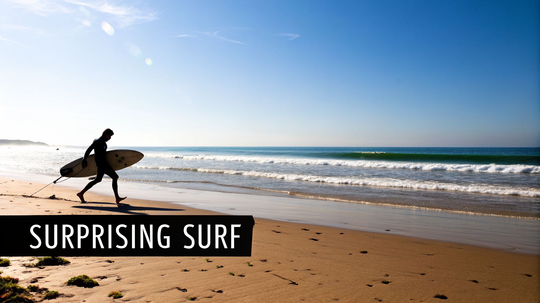 A surfer carries a surfboard while walking on a sunny sandy beach towards the blue ocean waves.