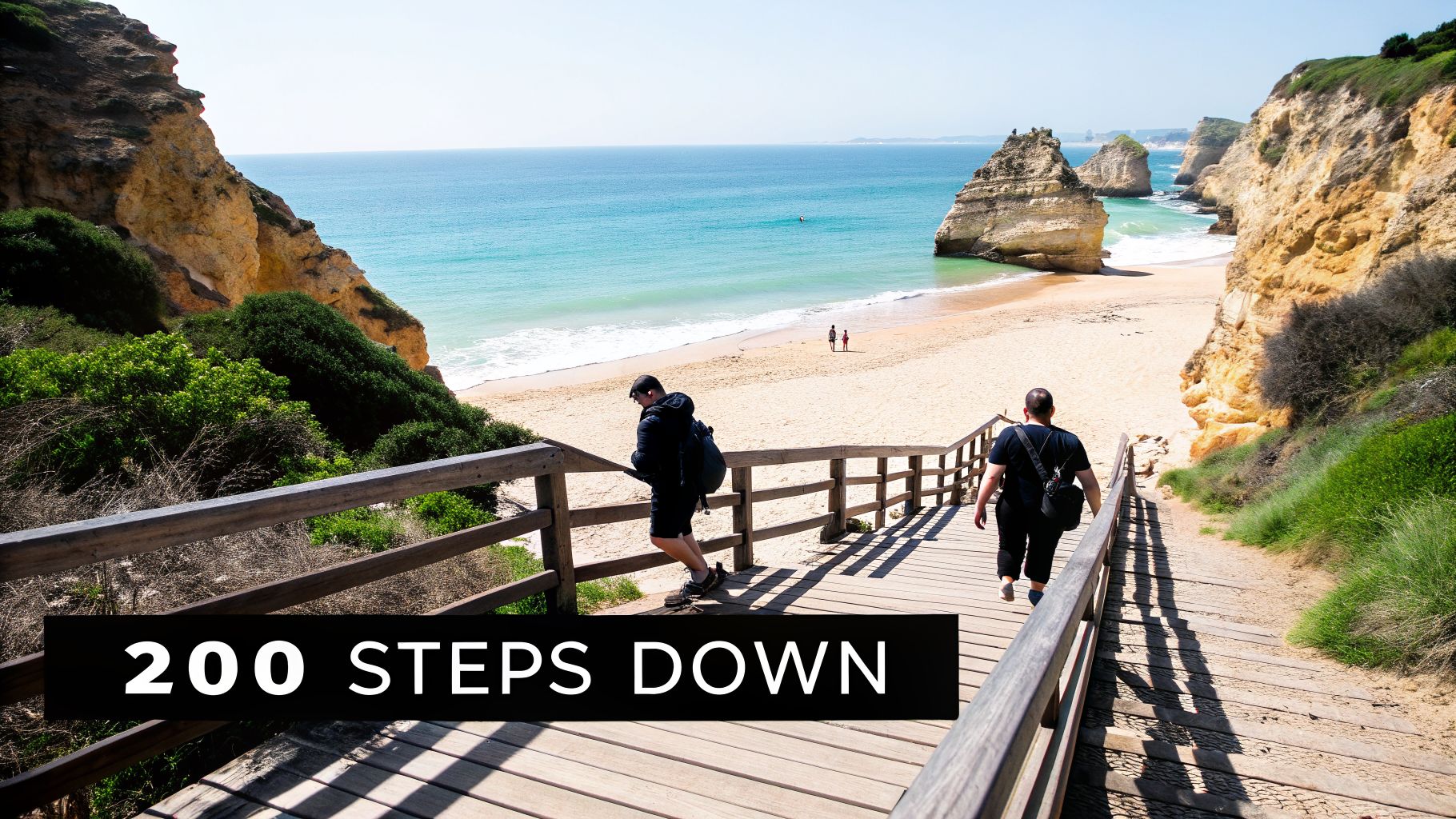 People walk down a long wooden staircase to a picturesque sandy beach with turquoise sea and rock formations.