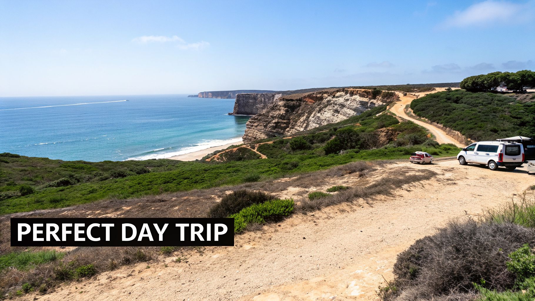 Panoramic coastal view with cliffs, a sandy beach, blue ocean, and a dirt road with two parked vehicles.