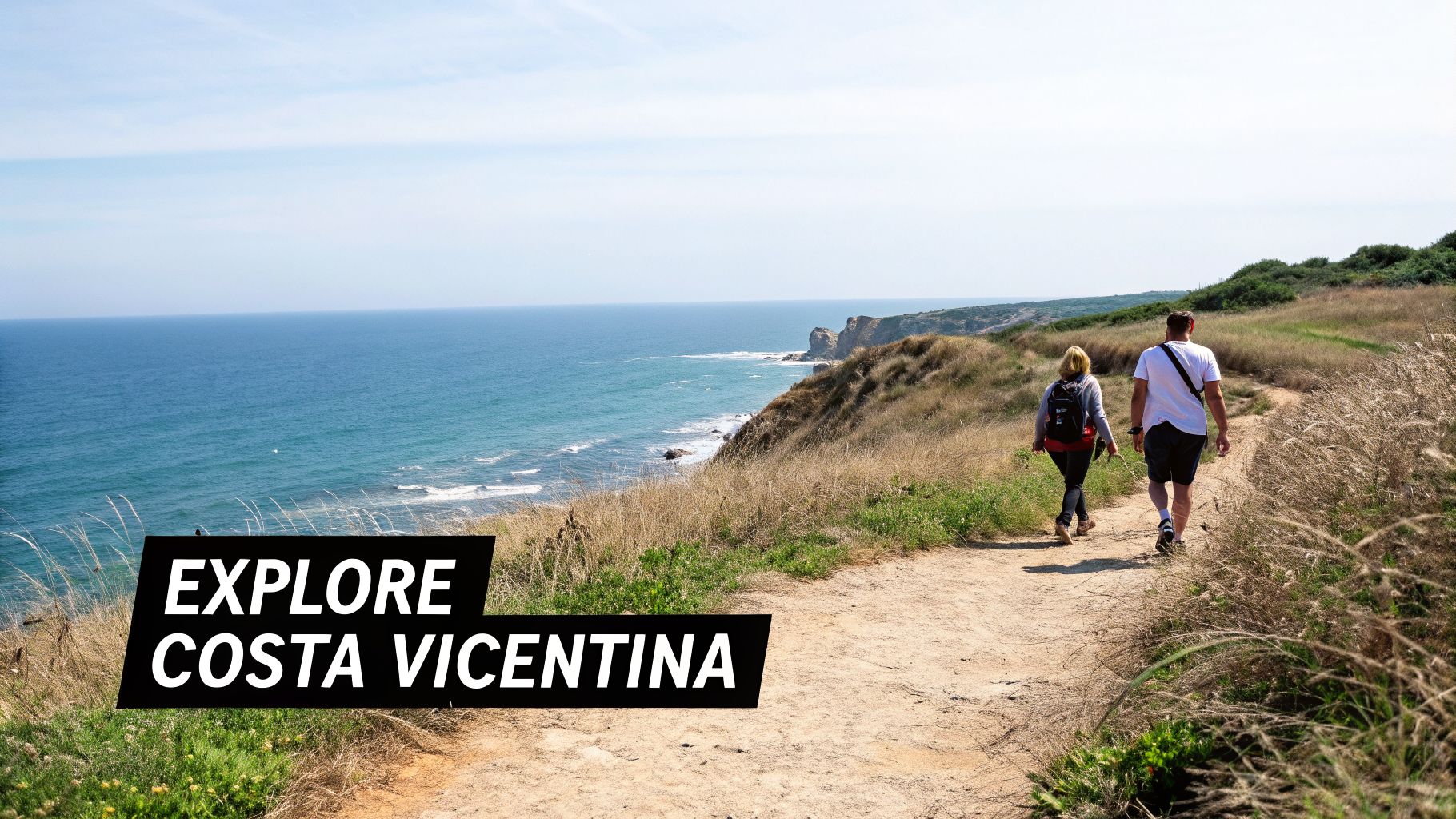 Two hikers walk a scenic coastal path overlooking the vast blue ocean and cliffs of Costa Vicentina.