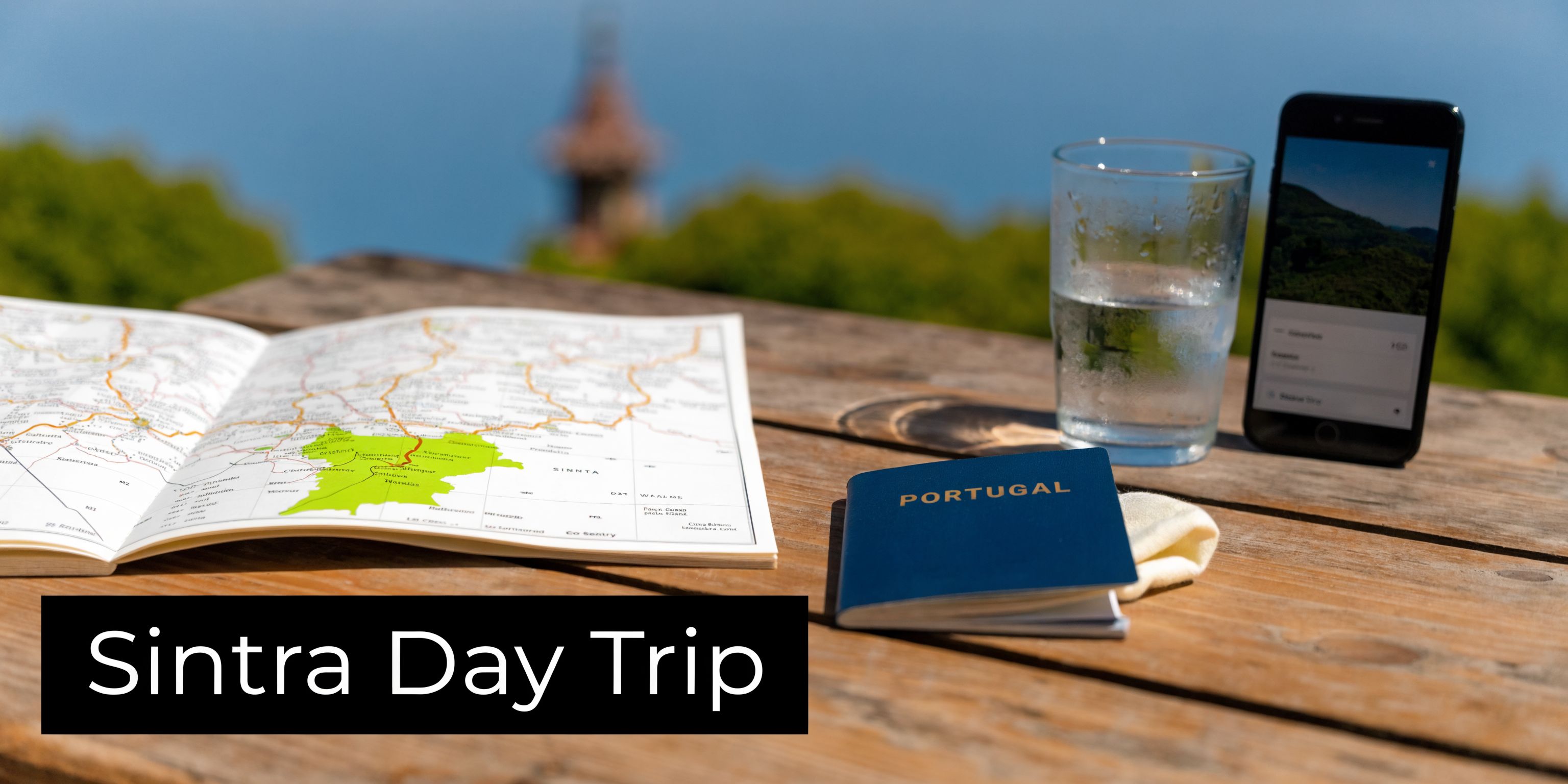 A passport, a map, and a smartphone on a wooden table overlooking a scenic landscape in Sintra.