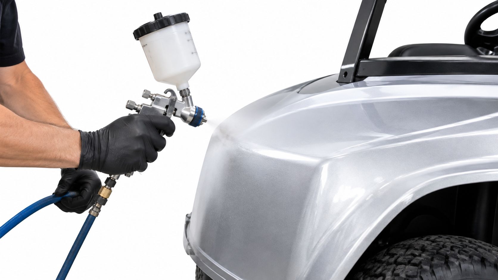 A person wearing black gloves using a paint spray gun to apply silver paint to a golf cart.
