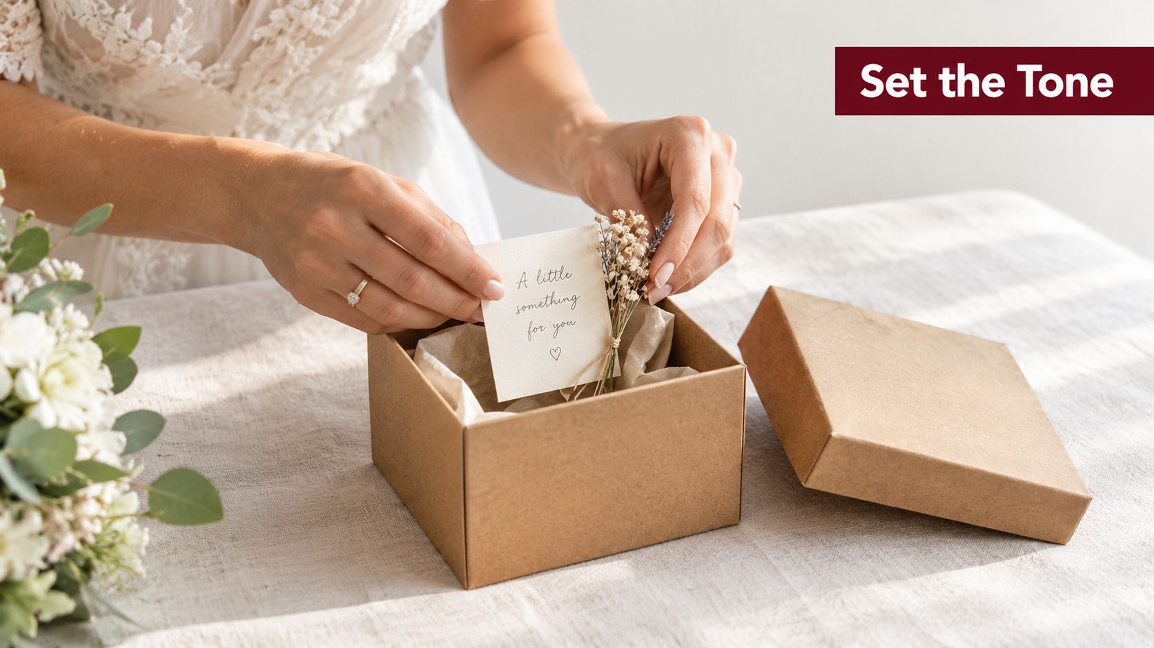 A woman holding a small personalized card over a gift box containing dried flowers and tissue paper.