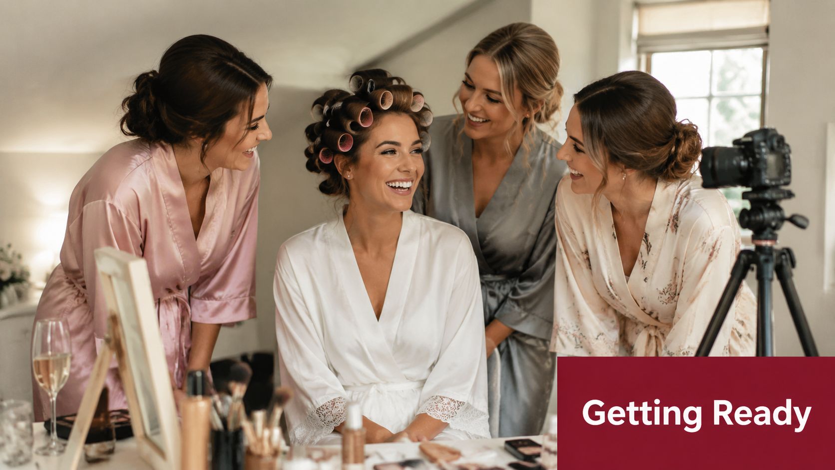 A happy bride wearing hair rollers and a white silk robe getting ready with her bridesmaids.