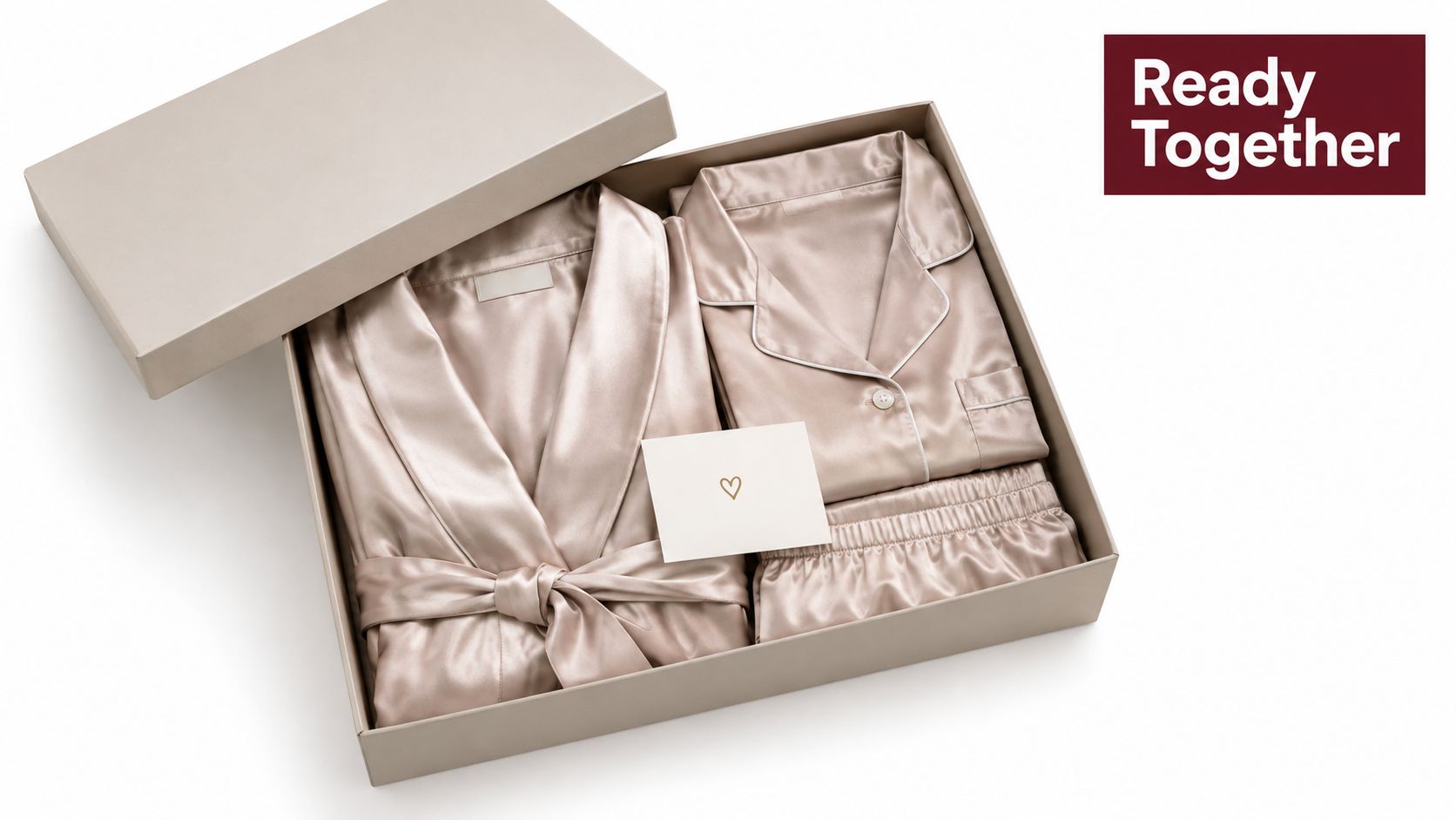 A sophisticated gift box containing champagne-colored satin pajamas and a robe, accompanied by a small love heart card.