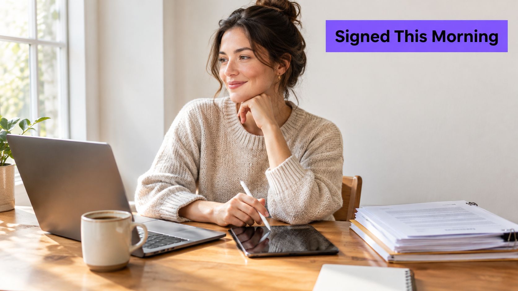 A woman working remotely at her desk, signing digital documents on a tablet next to a laptop.