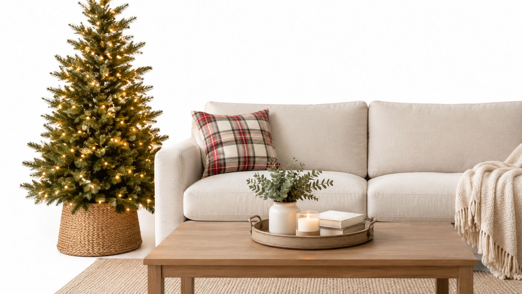 A cozy living room featuring a lit Christmas tree next to a neutral sofa with plaid pillows.