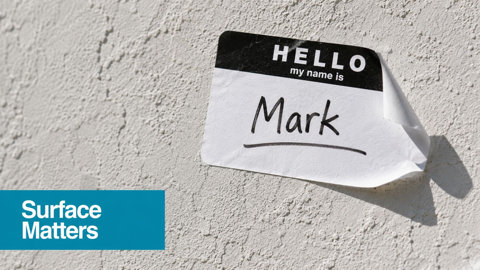 A name tag sticker labeled Mark is stuck on a textured off-white wall surface.