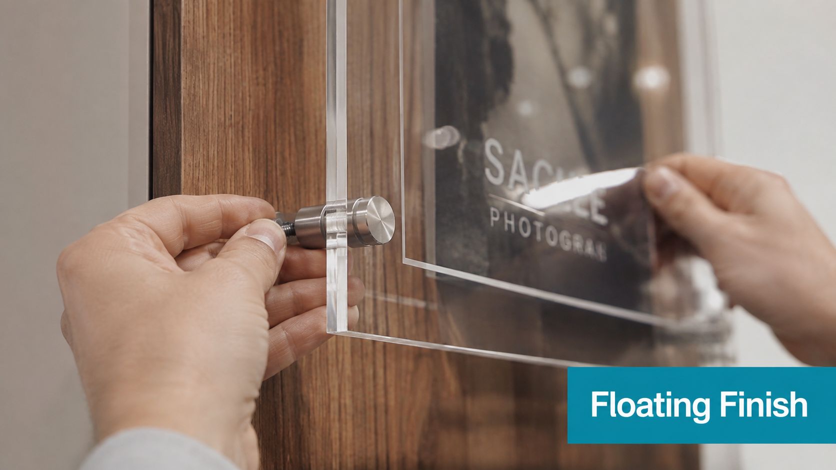 A pair of hands installing a modern acrylic photo display sign with silver mounting hardware on wood.