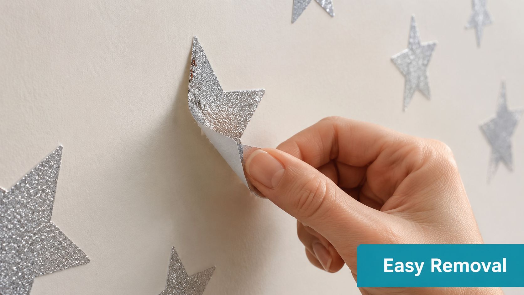A close-up view of a hand peeling a sparkling silver glitter star sticker off a wall.