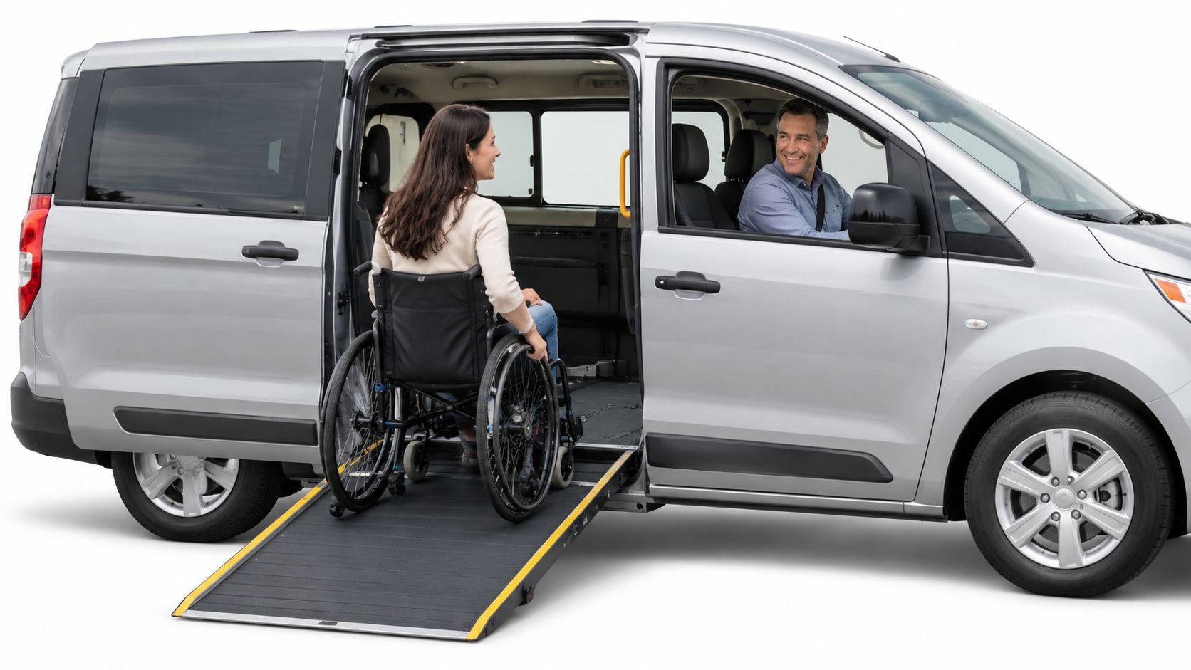 A woman in a wheelchair boarding a silver van using an accessible side door ramp while driver watches.