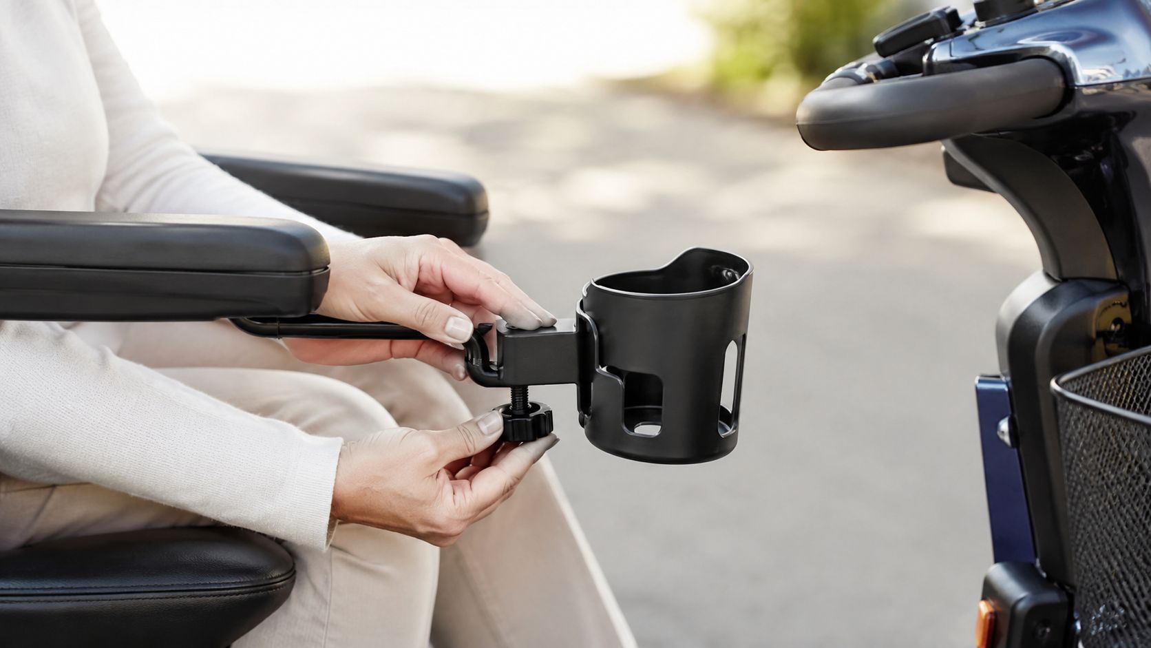 A person attaching a black cup holder accessory to the armrest of a mobility scooter.