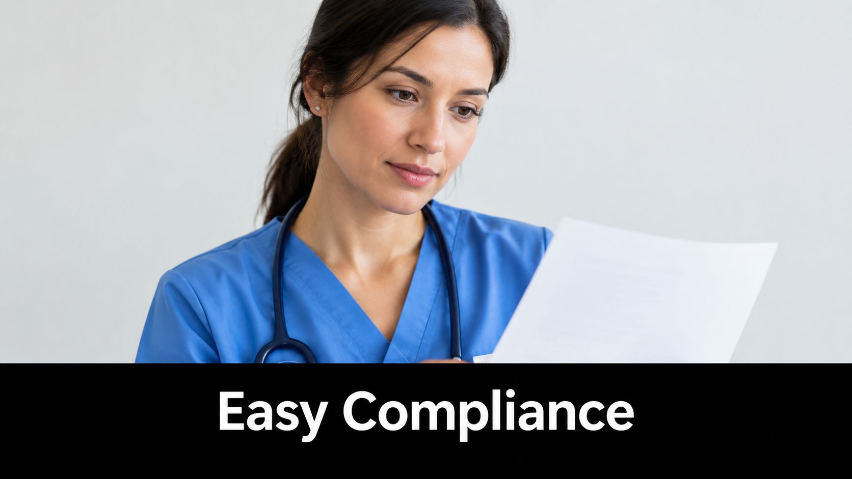 A female healthcare professional in blue scrubs reviewing medical documentation with a focused expression.