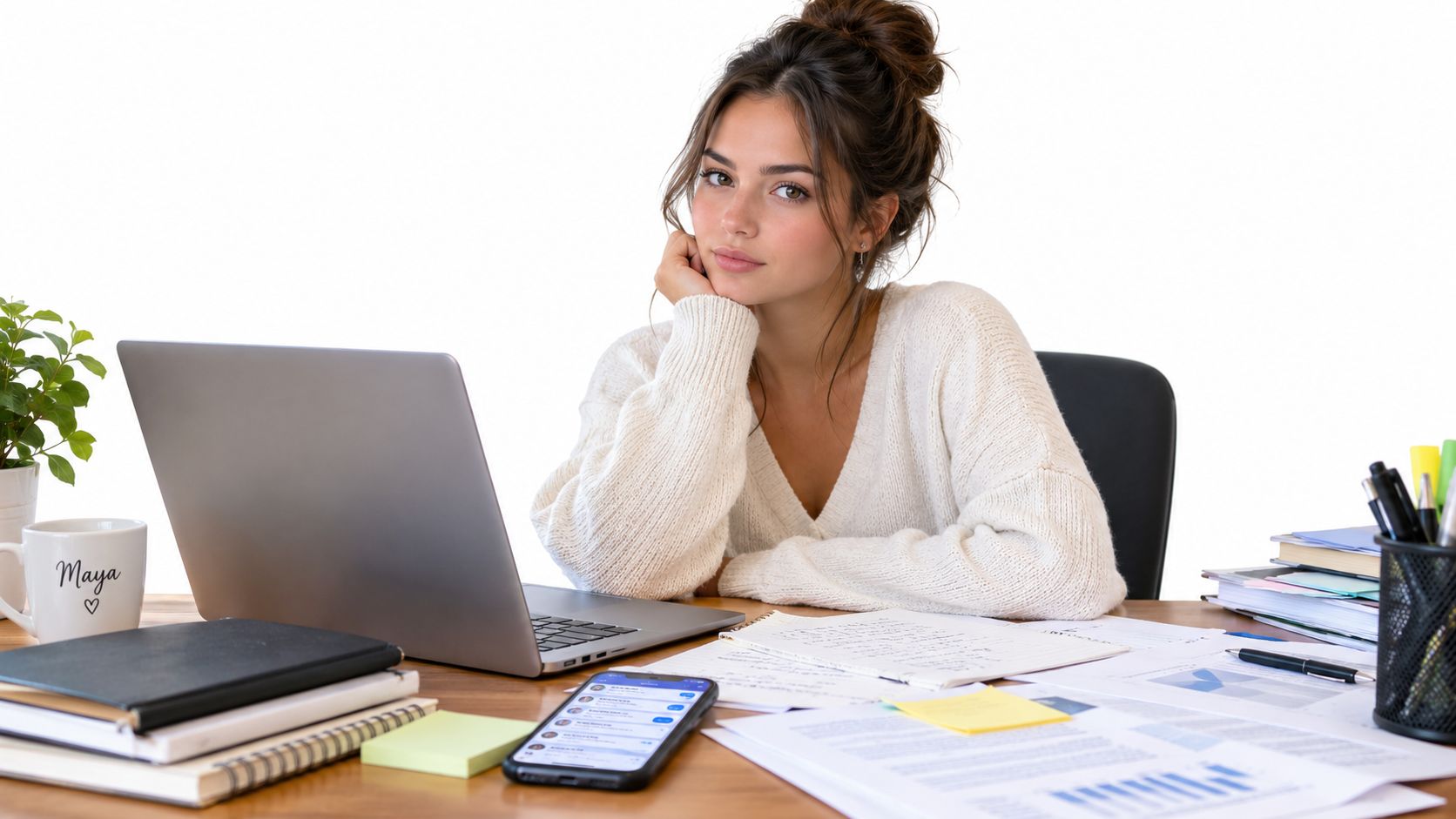 A young woman in a white sweater sitting at a desk with a laptop and documents.