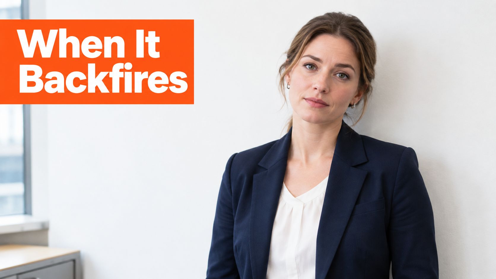 A professional woman in a navy blazer stands against a plain white wall looking concerned.