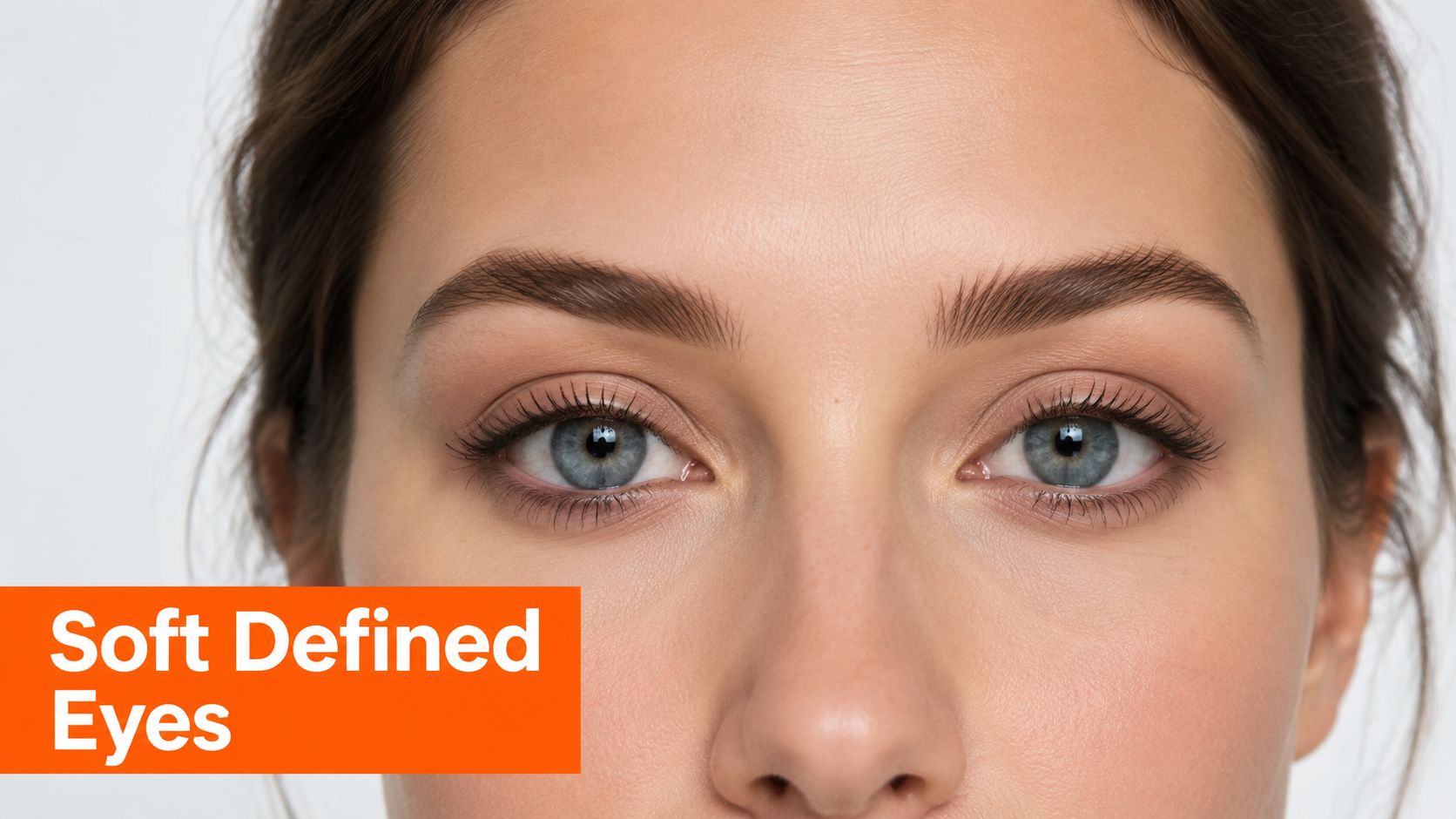 A close-up of a woman's face highlighting natural makeup with soft defined eyes and groomed brows.