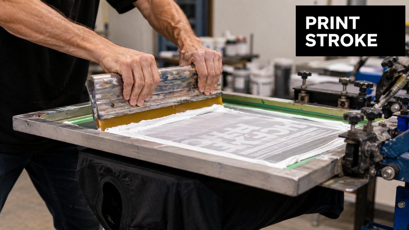 A professional printer uses a squeegee to apply white ink through a screen onto a t-shirt.
