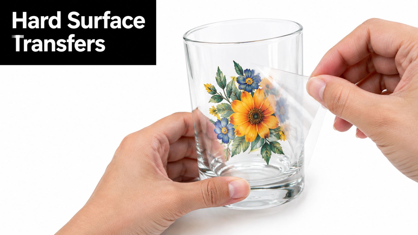 A person applying a colorful floral design decal onto a clear glass tumbler for customization.