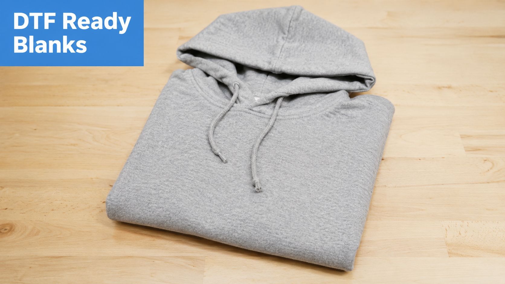 A neatly folded heather grey hooded sweatshirt rests on a light-colored wooden table surface.