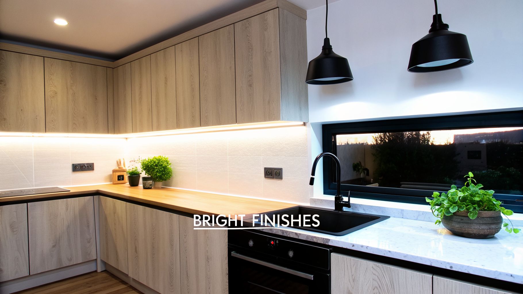 Modern kitchen with light wood cabinets, bright under-cabinet lighting, black sink, and sunset view.