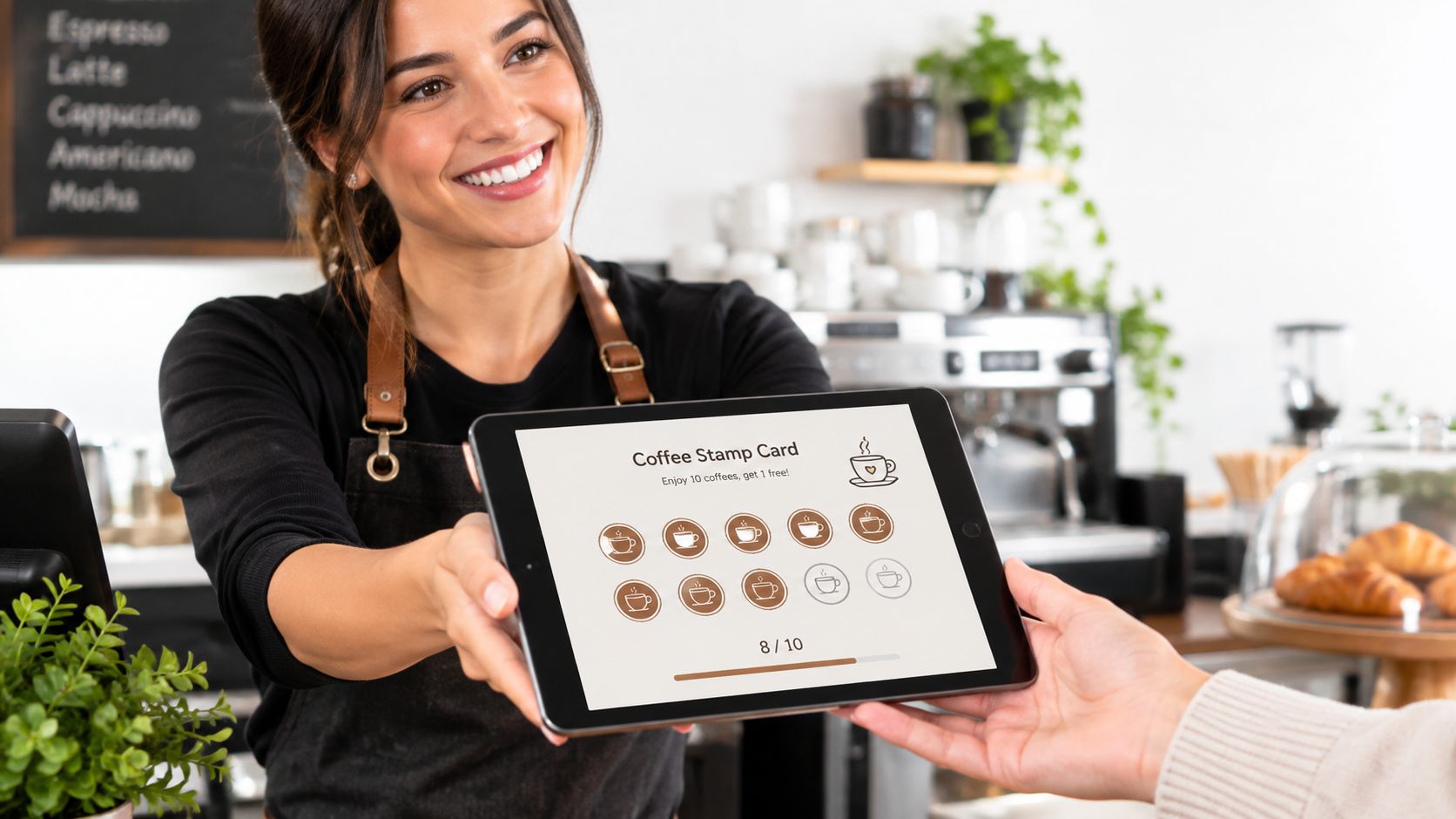 A friendly barista holding a digital tablet displaying a coffee loyalty stamp card to a customer.