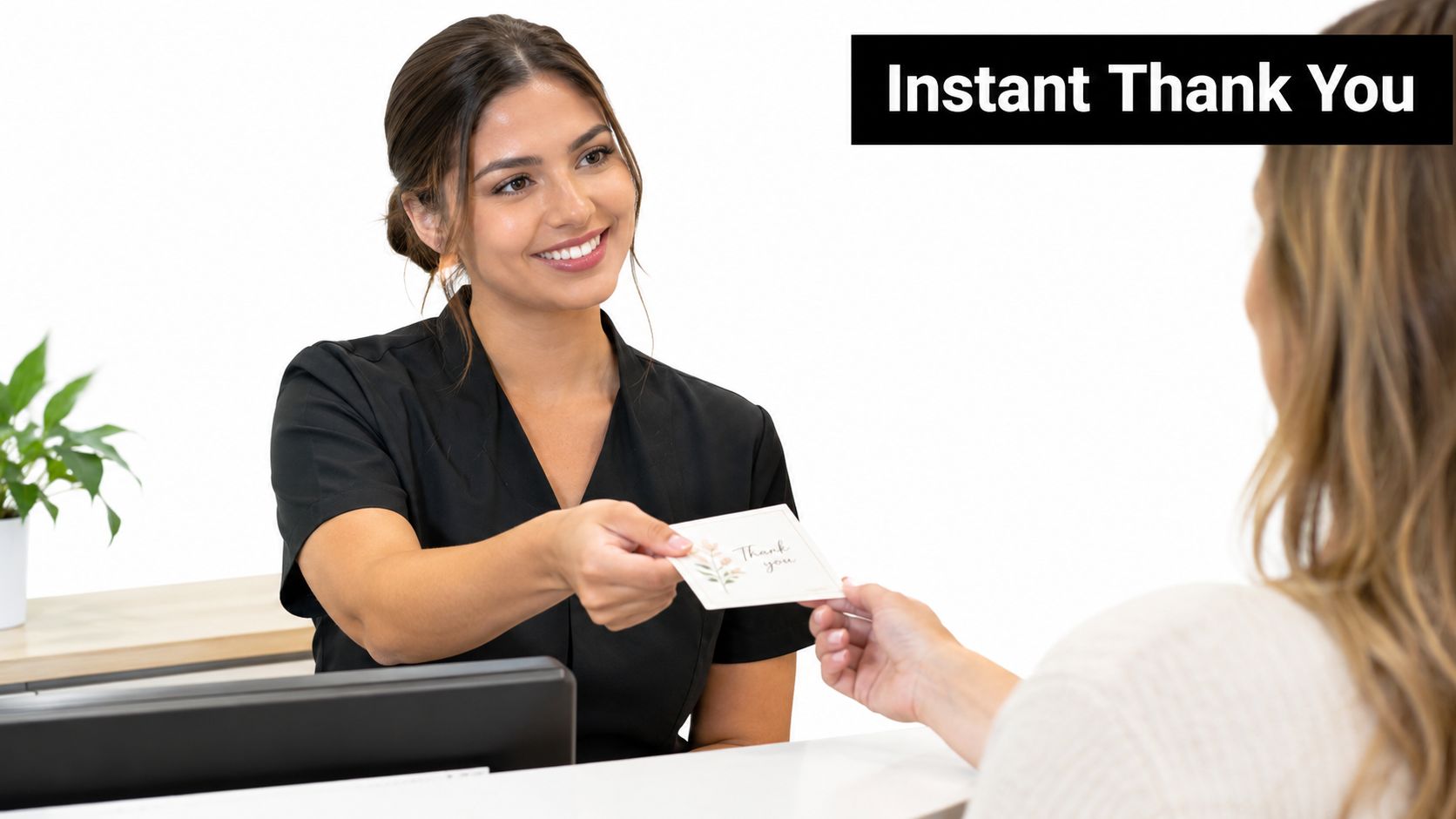 A smiling receptionist in a black uniform hands a thank you card to a customer at a desk.