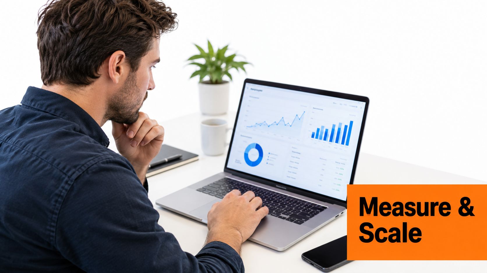 A man working on a laptop at a white desk reviewing business data analytics and performance charts.