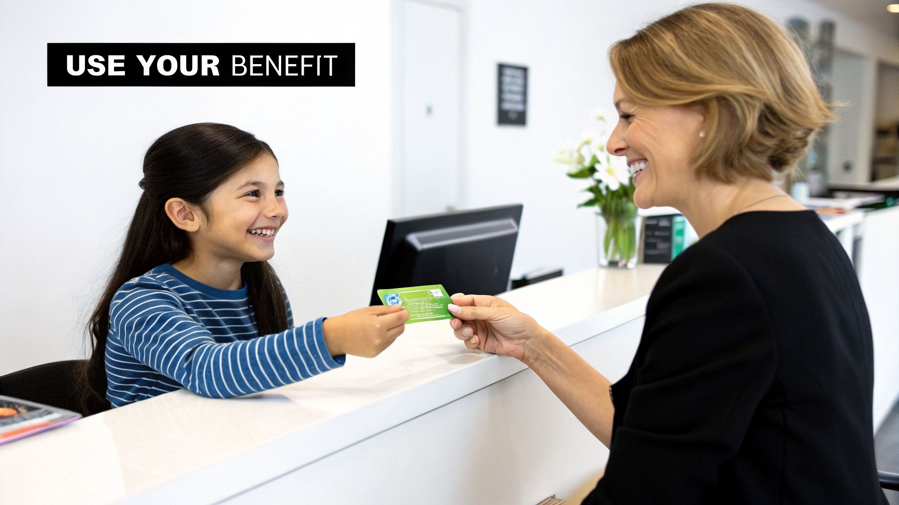 A smiling young girl hands a green benefit card to a friendly receptionist at a clinic or office.