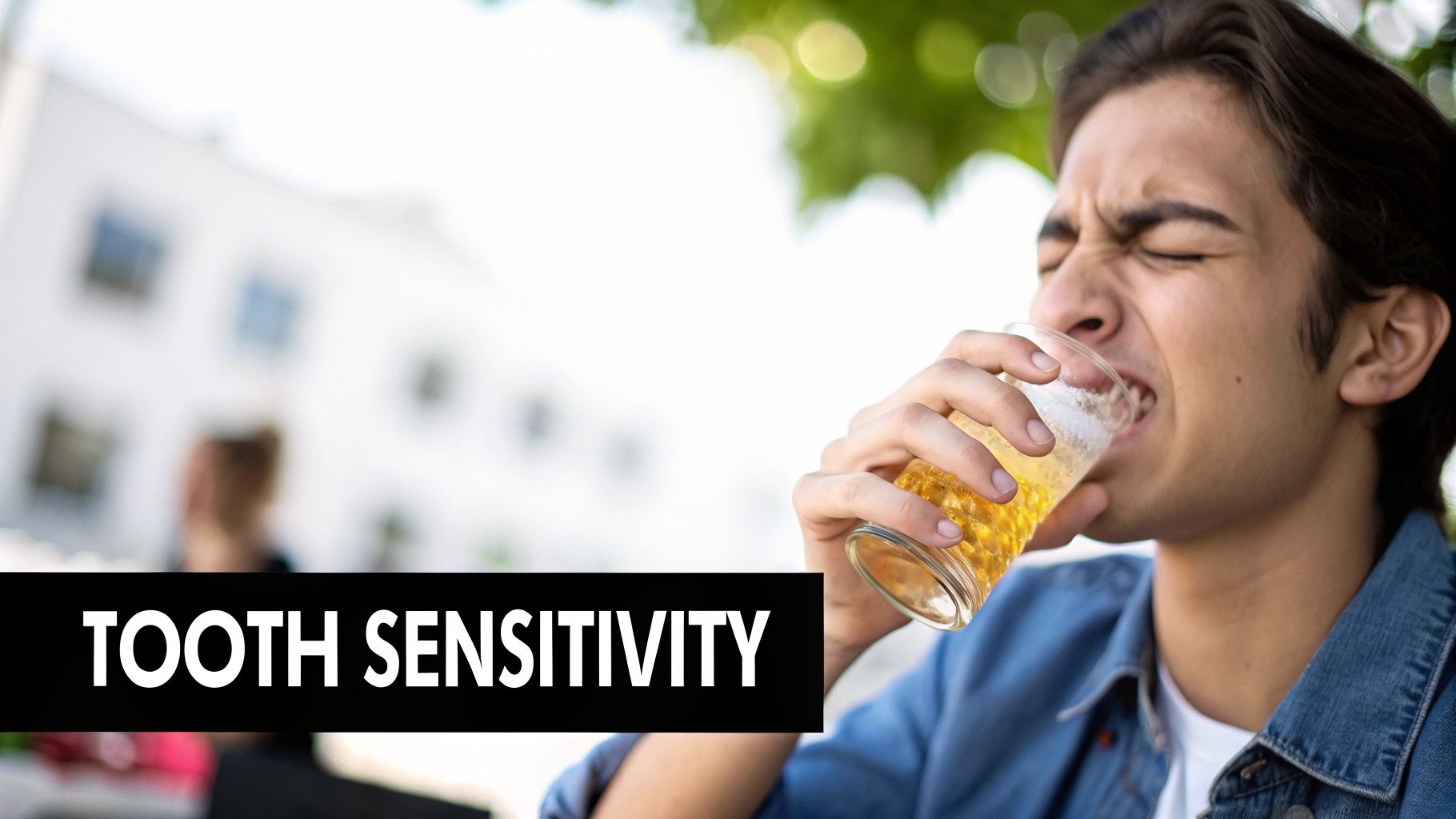 A young man winces in pain while drinking a cold beverage from a glass, indicating tooth sensitivity.